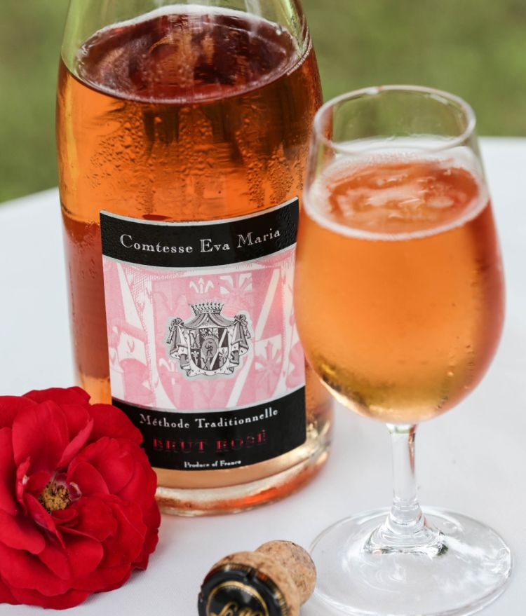 Gefülltes Rosé-Weinglas vor der gekühlten Flasche mit Blumendecko